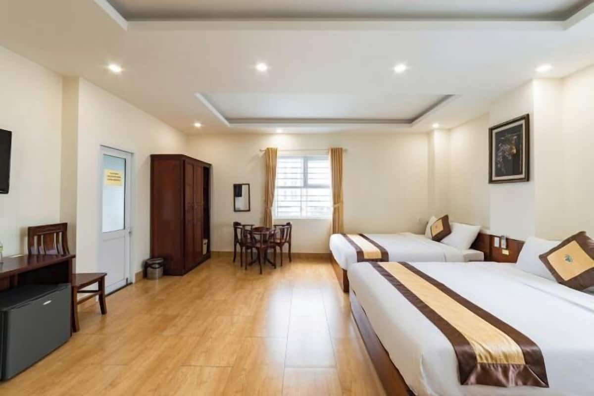 Une chambre d’hôtel avec deux lits, un bureau, une chaise, une petite table, une armoire et une fenêtre avec des rideaux.