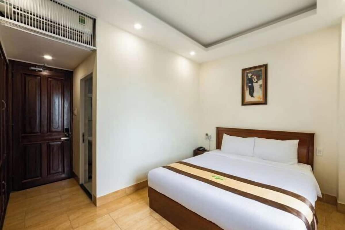 Une chambre d’hôtel avec un lit, une table de chevet, un tableau au mur et une porte en bois.