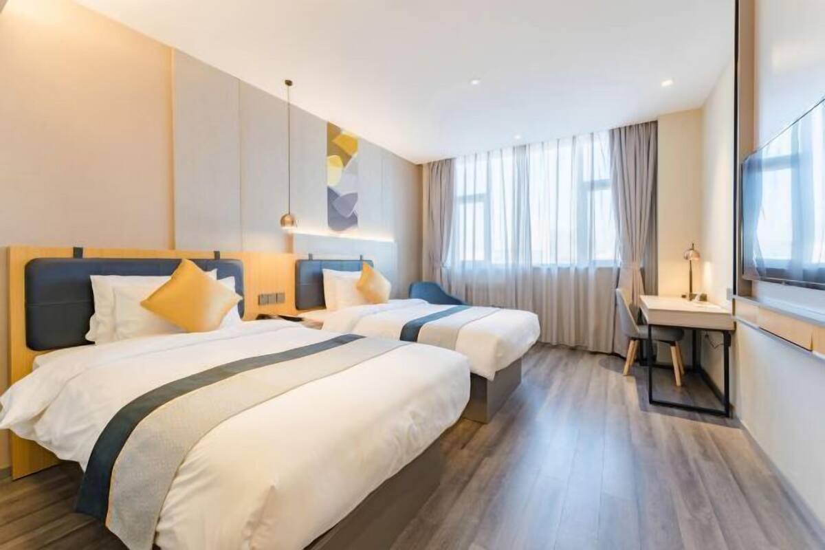 A hotel room with two beds, a desk, a chair, and a large window with curtains.