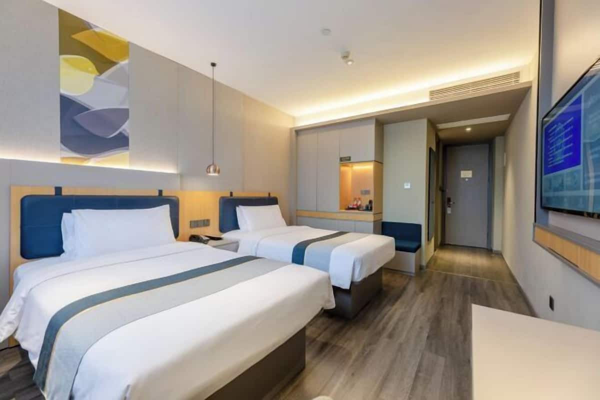 A hotel room with two beds, a desk, a mirror, and a TV.