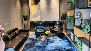 A modern lobby with a black leather sofa, two black armchairs, a round coffee table, and a bookshelf with plants. - Homeinn Selected Hotel (Zhengzhou Huayuan Road Grand Emporium) (Zhengzhou)
