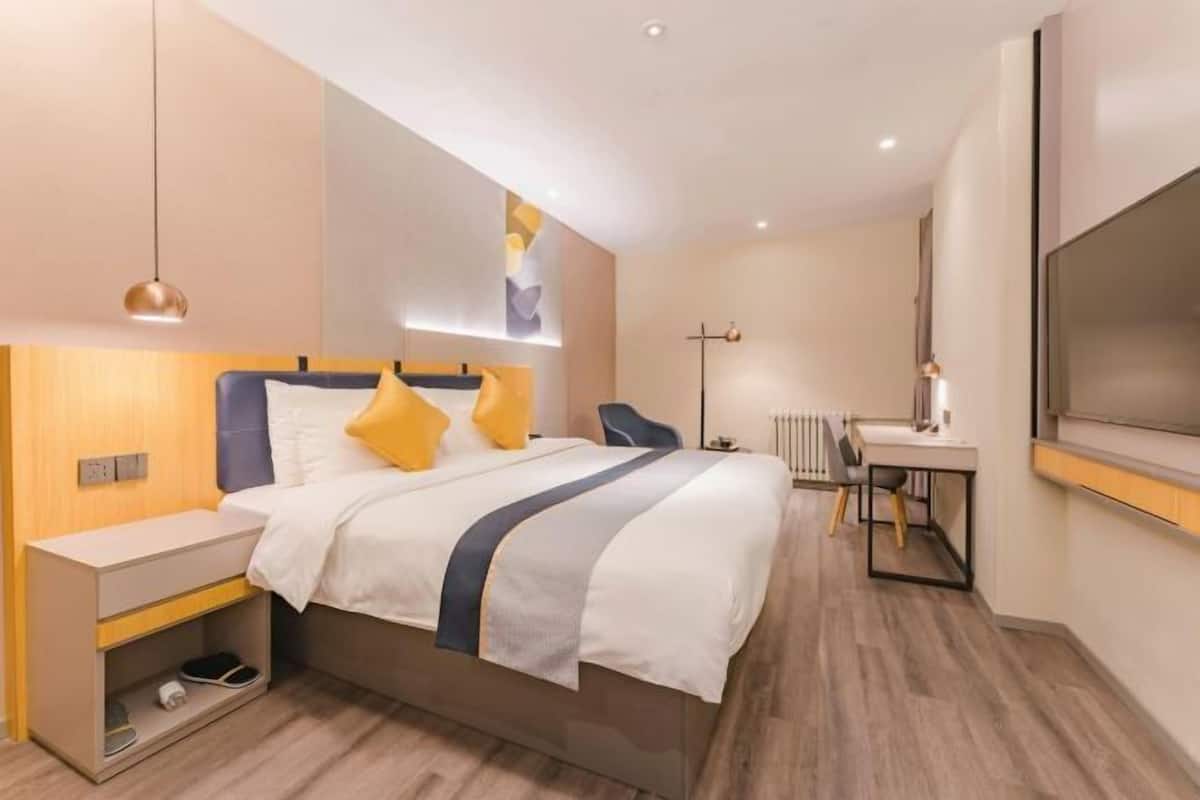 A modern hotel room with a bed, bedside table, desk, and a TV.
