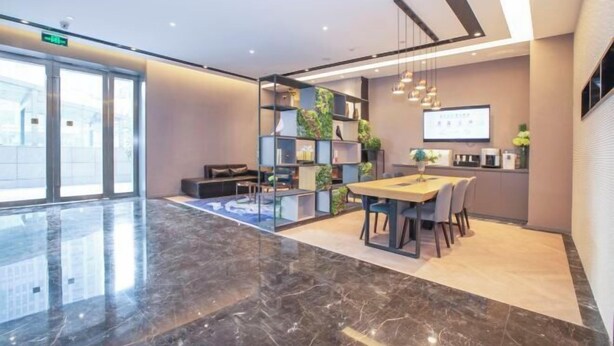 A modern hotel lobby with a marble floor, a reception desk, a dining area with a wooden table, and a wall with shelves and plants. - Homeinn Selected Hotel (Zhengzhou Huayuan Road Grand Emporium) (Zhengzhou)