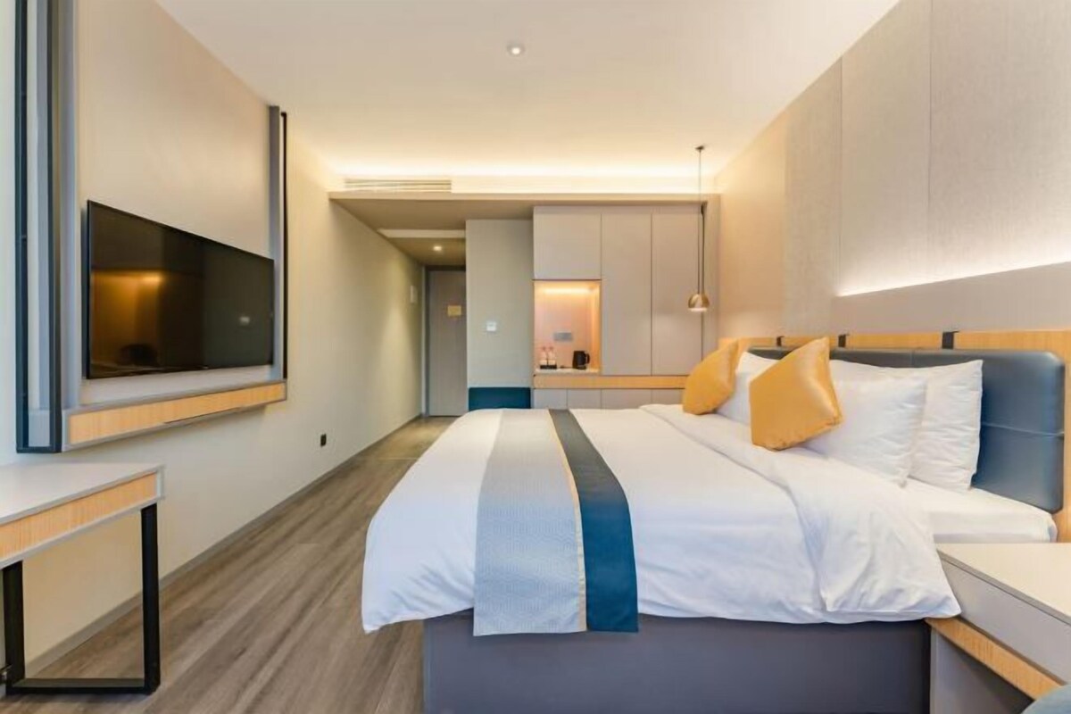 A modern hotel room with a large bed, a flat-screen TV, a bedside table, and a built-in wardrobe.