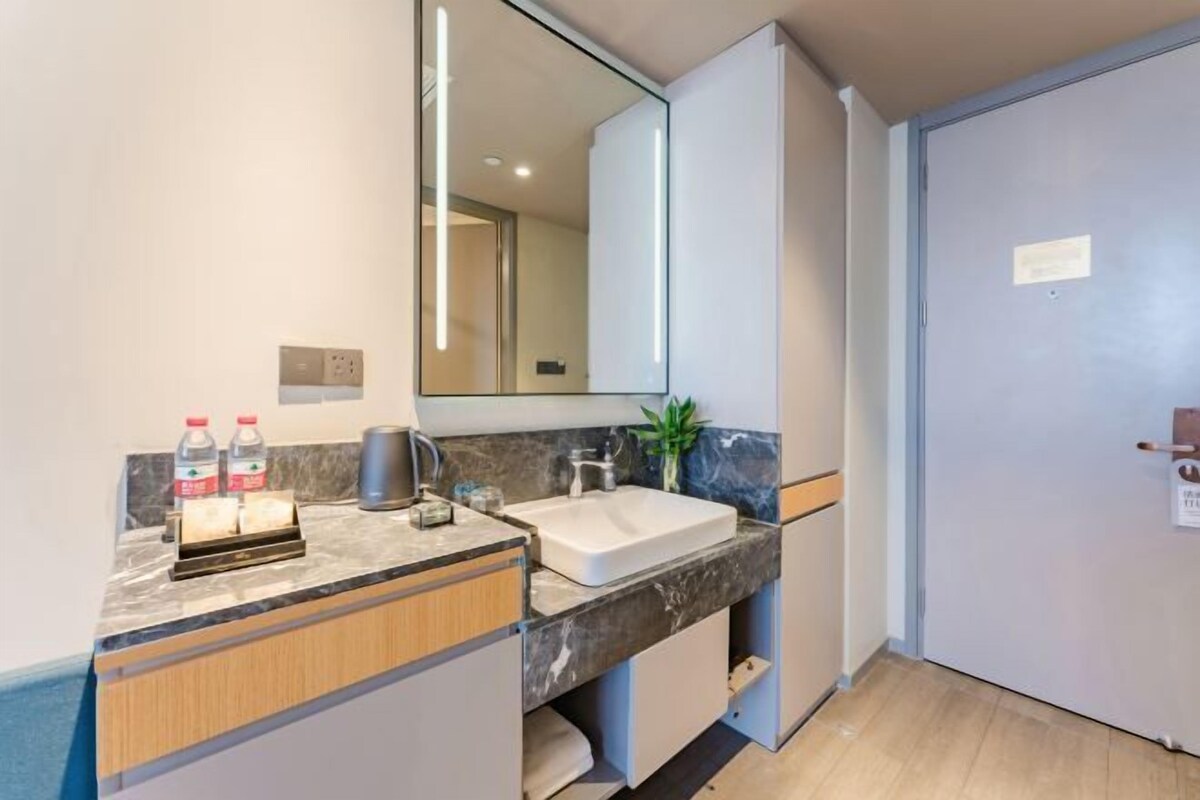 A modern bathroom with a marble countertop, a sink, a mirror, and a door.