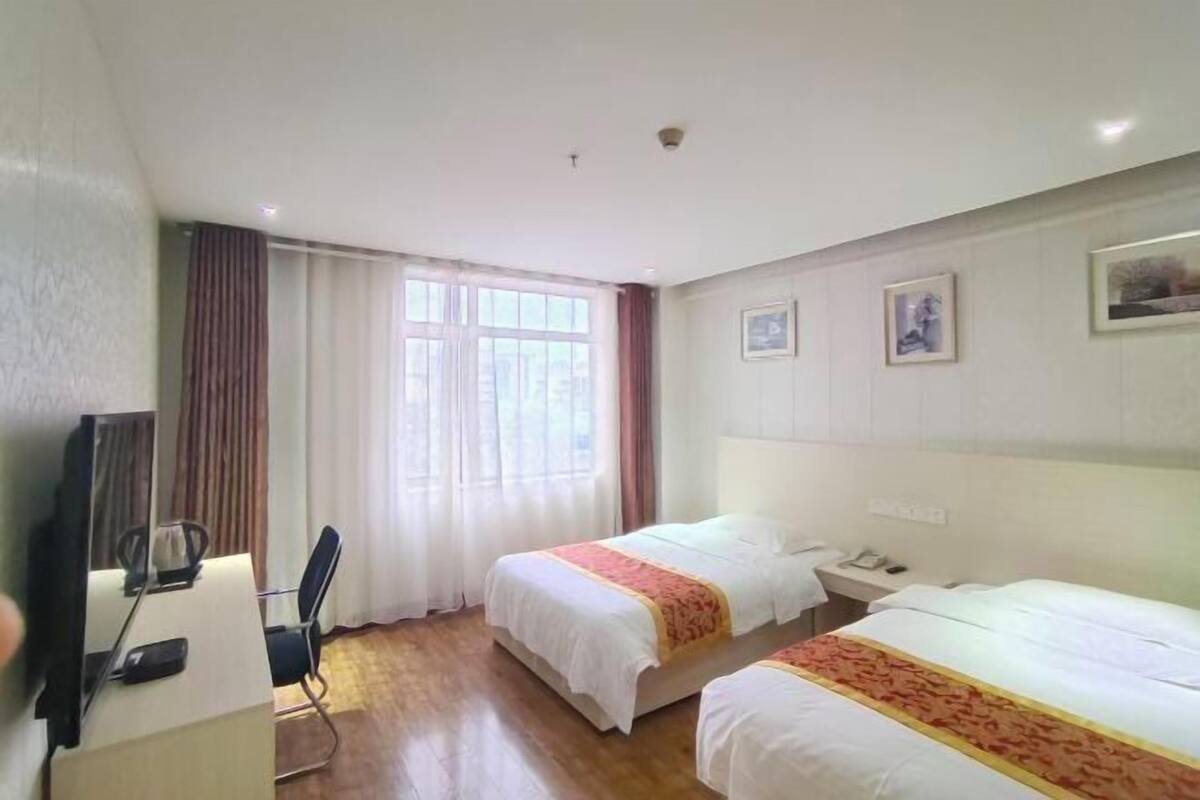 Hotellihuone, jossa on kaksi sänkyä, työpöytä tuolilla, televisio ja ikkuna, jossa on verhot.