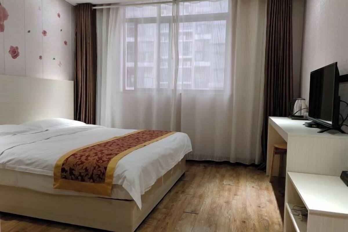 Hotellihuone, jossa on sänky, työpöytä tietokoneella ja ikkuna, jossa on verhot.