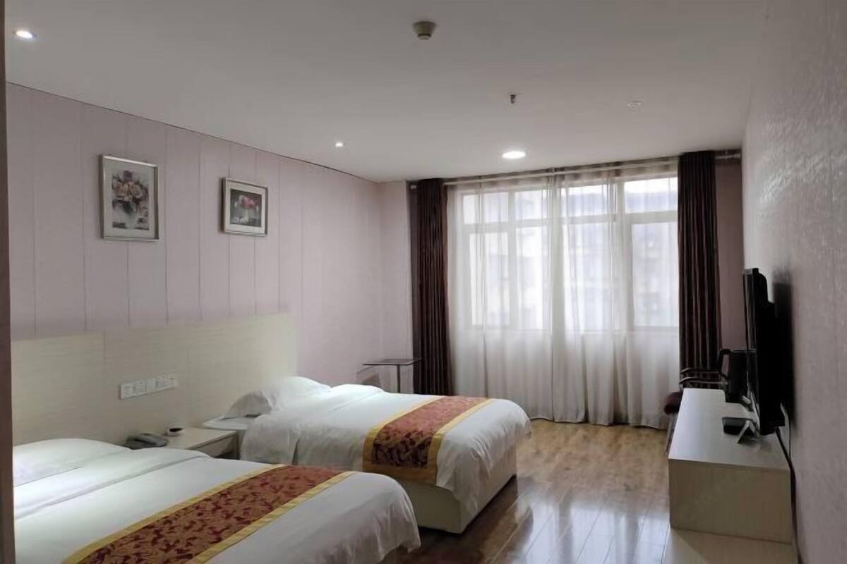 Hotellihuone, jossa on kaksi sänkyä, työpöytä tietokoneella, televisio ja ikkuna, jossa on verhot.