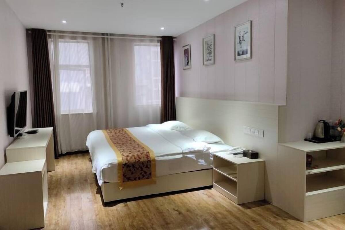 Hotellihuone, jossa on sänky, yöpöydät, televisio ja verhot.