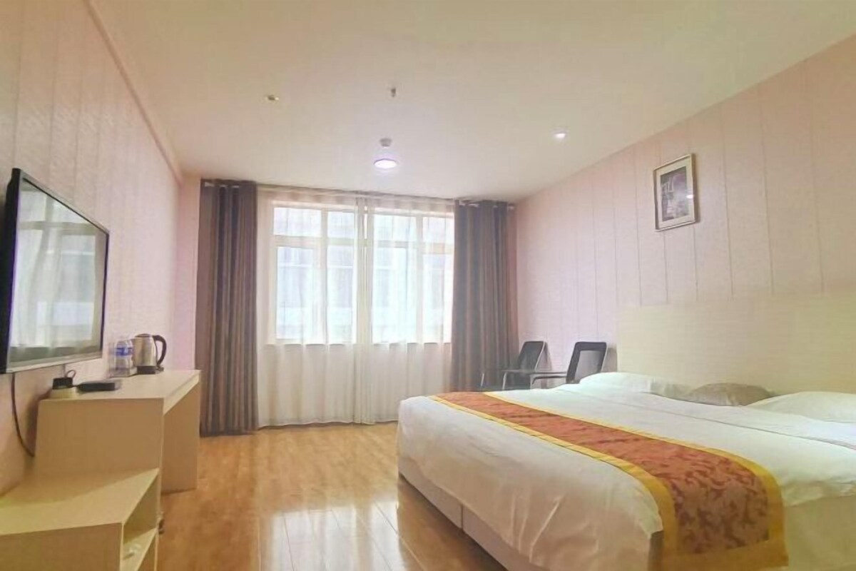 A hotel room with a bed, a desk with a television, and a window with curtains.