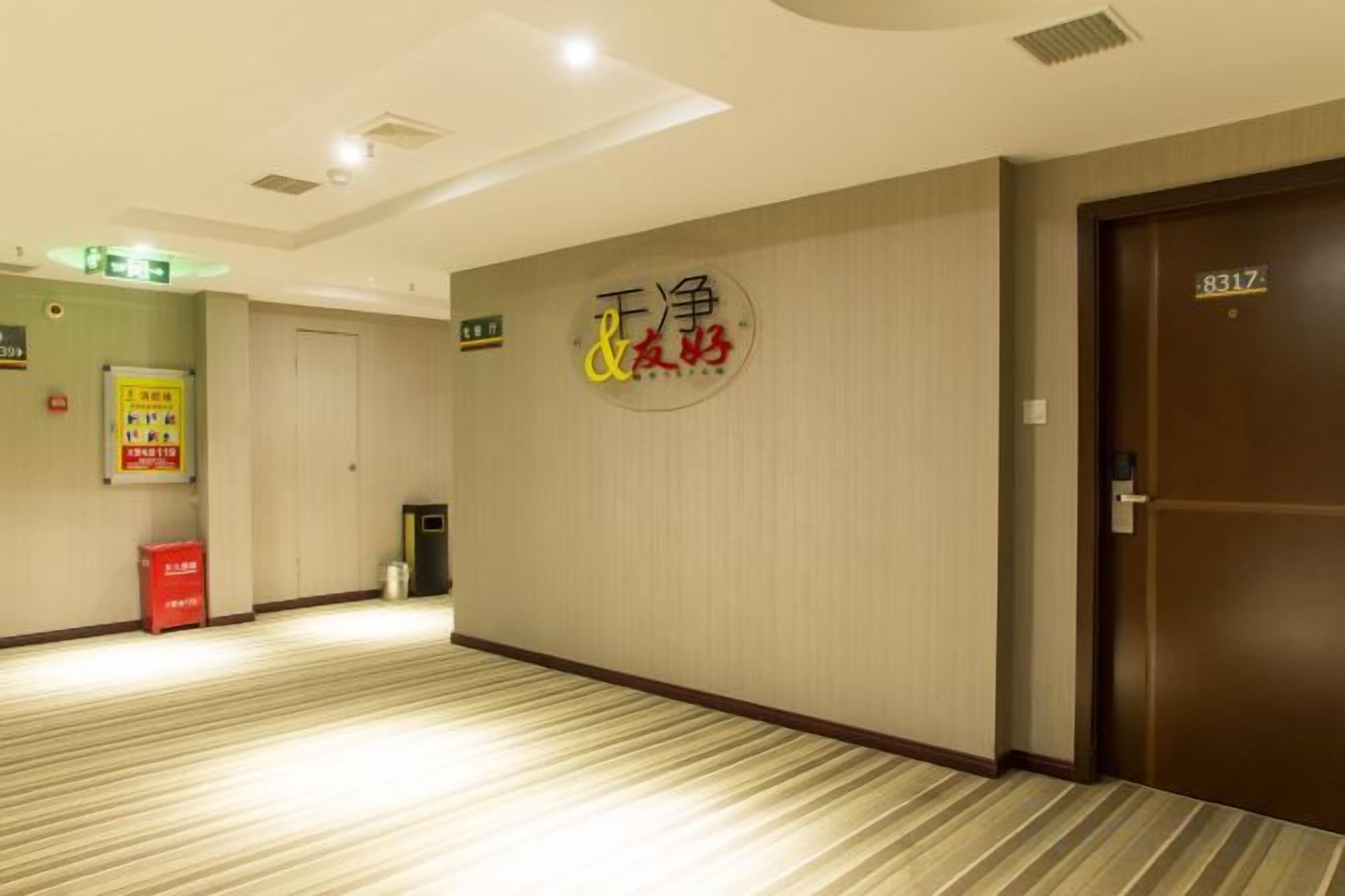 A hotel corridor with a carpeted floor, a door with a number sign, and a wall with a sign.