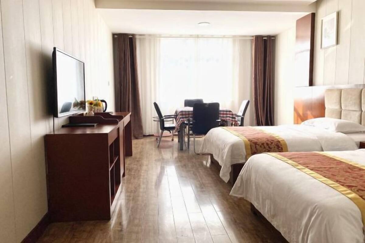 Hotellihuone, jossa on kaksi sänkyä, työpöytä tuolilla, televisio ja ikkuna, jossa on verhot.