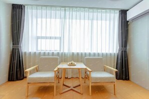Une pièce avec un plancher en bois, deux chaises, une petite table et une fenêtre ornée de rideaux légers.