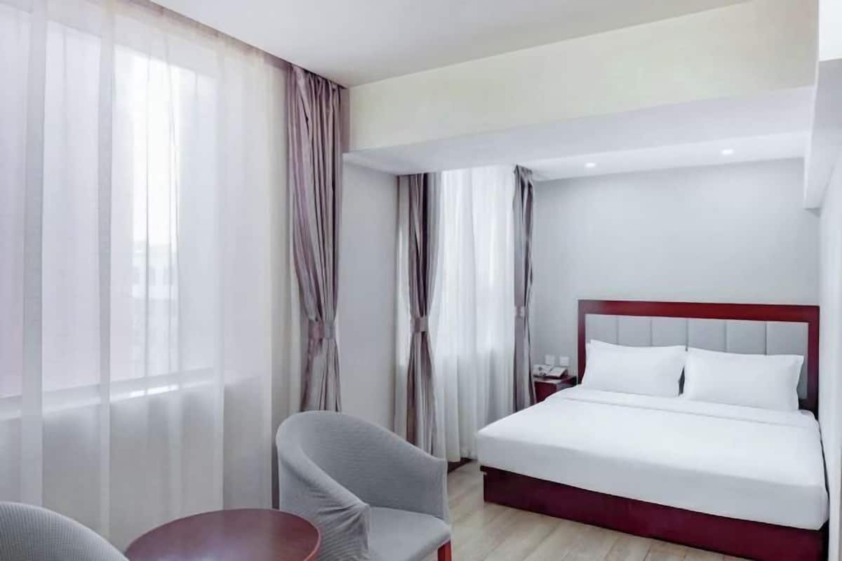 A hotel room with a bed, a chair, a small table, and curtains.