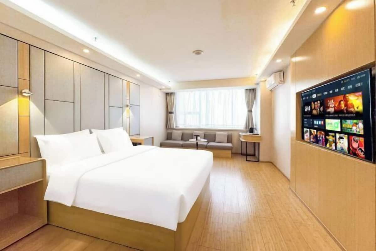 A hotel room with a bed, a sofa, a TV, and a wall-mounted screen displaying content.