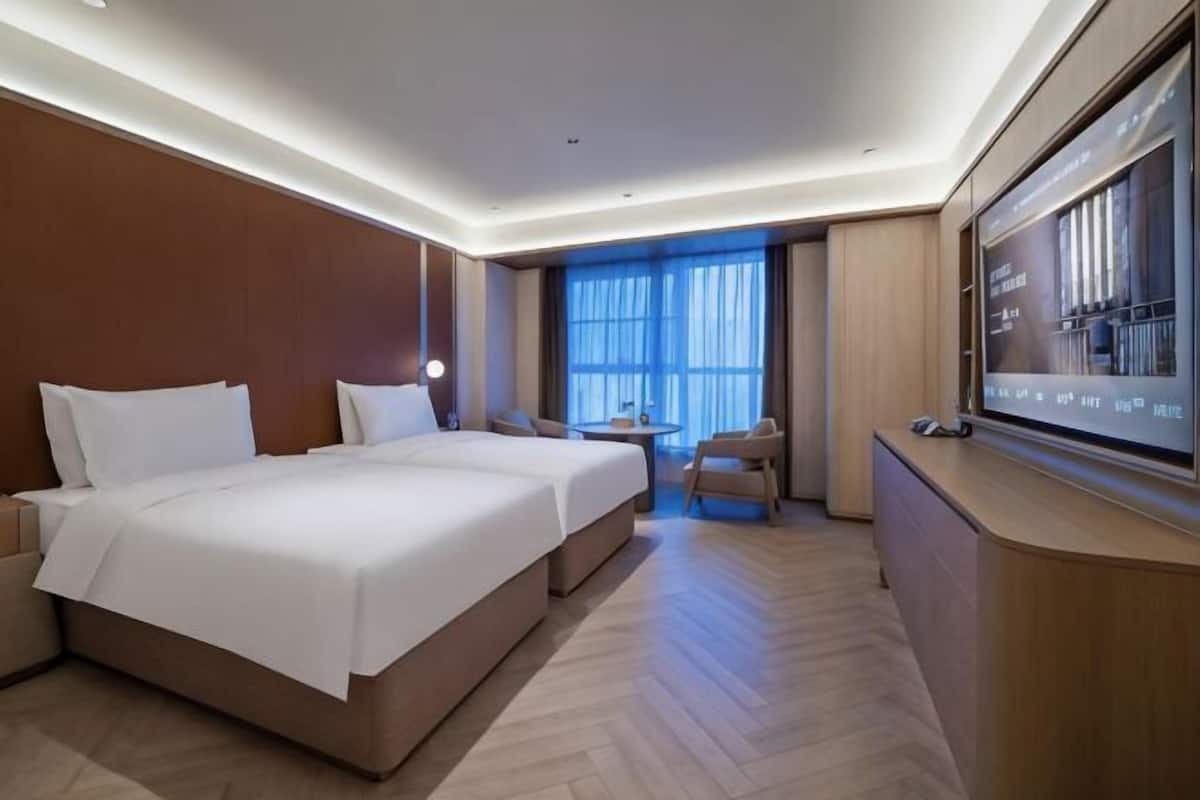 A hotel room with two beds, a desk, a chair, a TV, and a large window.