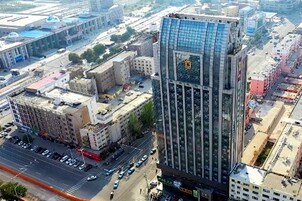 Um edifício alto com fachada de vidro, cercado por outros edifícios e uma rua movimentada.