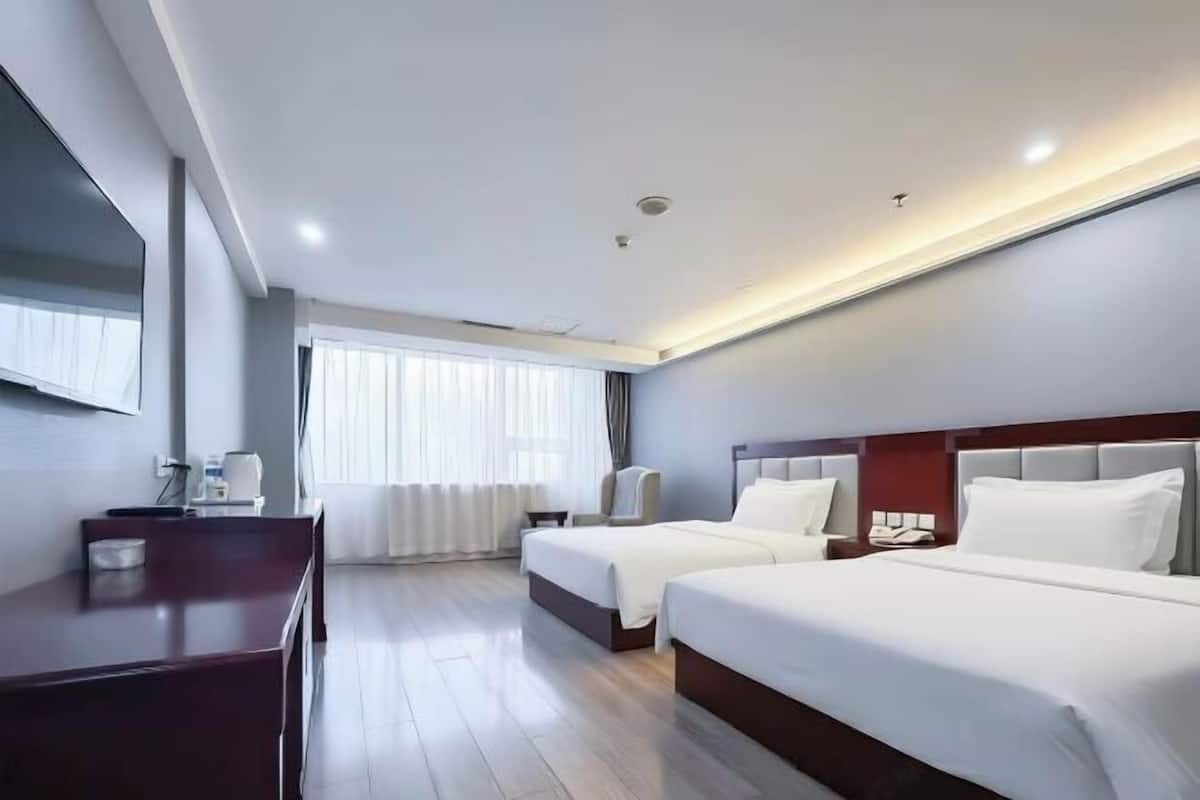 A hotel room with two beds, a desk, a chair, a TV, and a window with curtains.