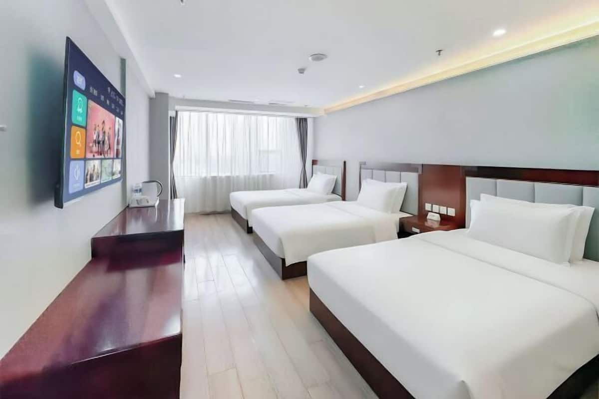 A hotel room with two beds, a desk, a TV, and a window with curtains.