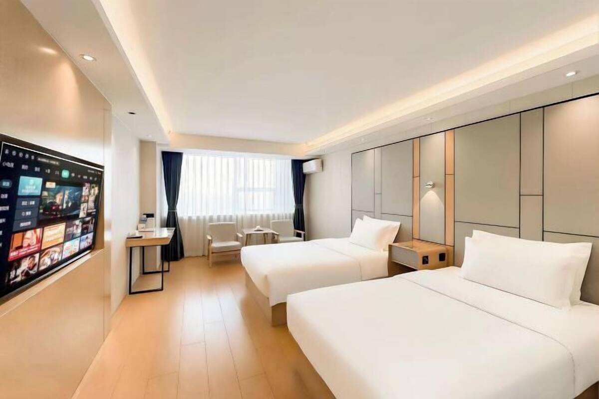 A hotel room with two beds, a desk, a TV, and a window with curtains.