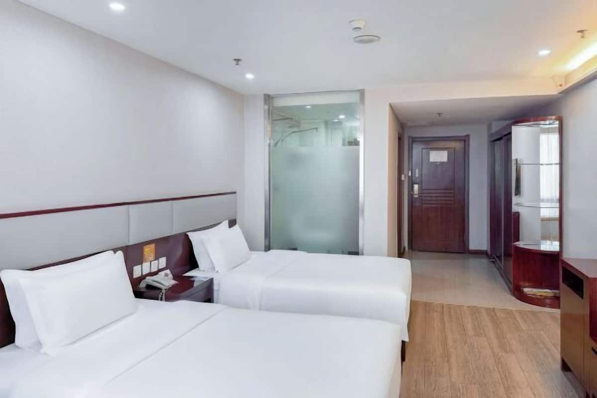 A hotel room with two beds, a wooden floor, a glass shower enclosure, and a wooden wardrobe.