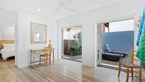 A spacious room with a wooden floor, a bed, a desk with a chair, and a view of an outdoor area with a pool and lounge chairs.