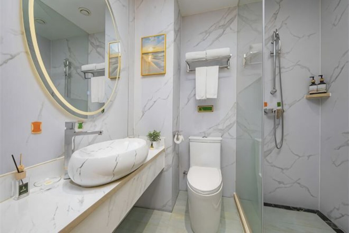 Et badeværelse med et marmorbadeværelse, et toilet, en glas brusekabine og et spejl med gylden ramme.