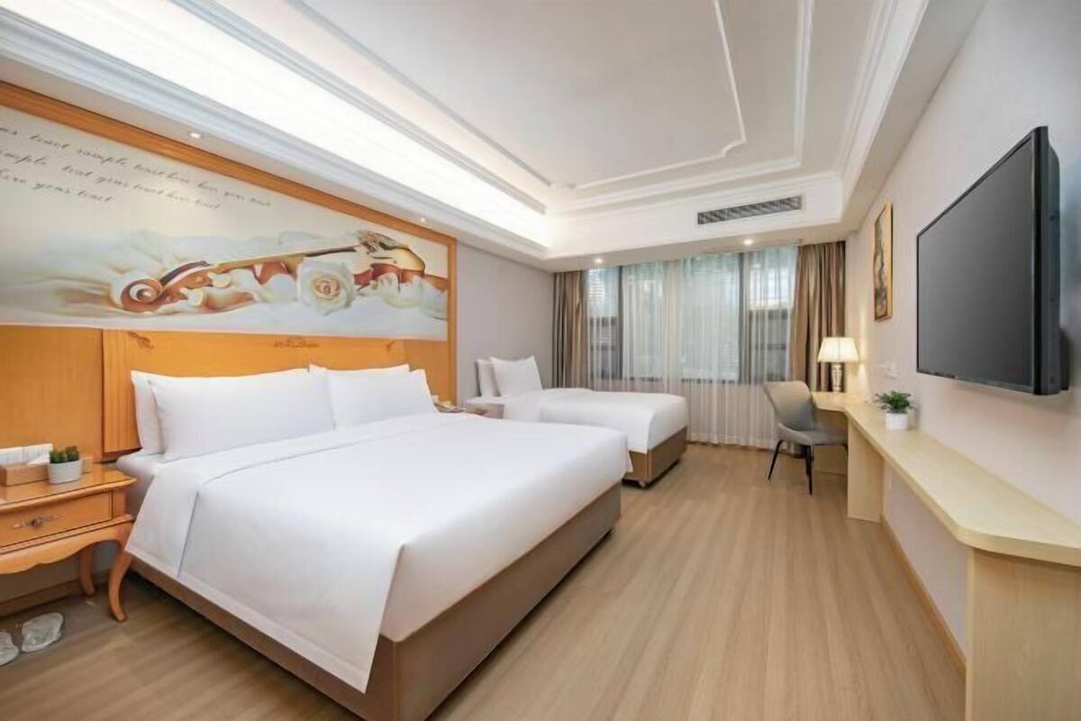 A hotel room with a large bed, a smaller bed, a desk, a chair, a TV, and a painting on the wall.