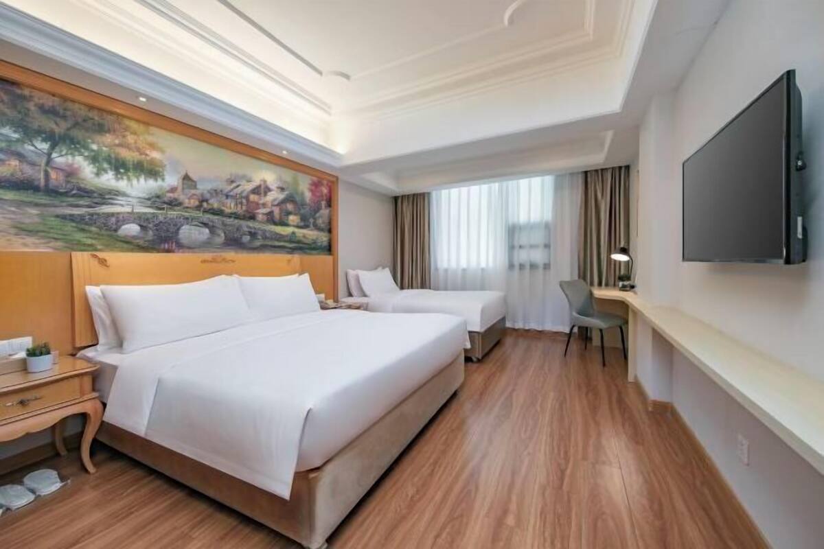 A hotel room with a large bed, a desk, a chair, a flat-screen TV, and a painting on the wall.
