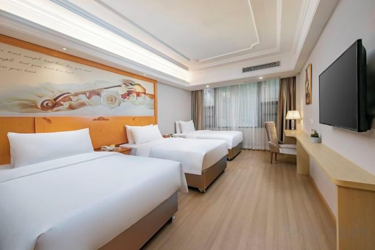 A hotel room with two beds, a TV, a desk, and a large window.