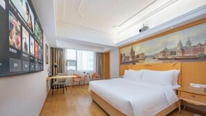 A hotel room with a large bed, a desk with two chairs, a painting on the wall, and a window with curtains. - Vienna International Hotel (Fuzhou)