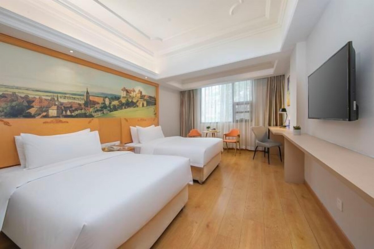 A hotel room with two beds, a desk, a chair, a TV, and a painting on the wall.