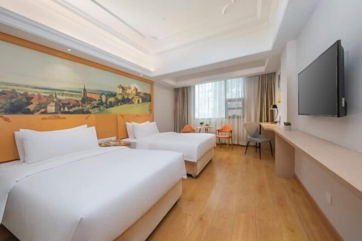 A hotel room with two beds, a desk, a chair, a TV, and a painting on the wall.