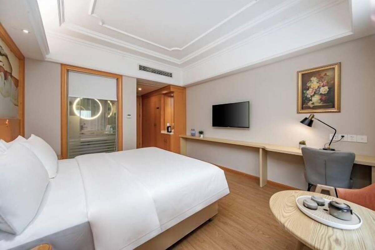 A hotel room with a bed, a desk, a television, and a small table with a tray.
