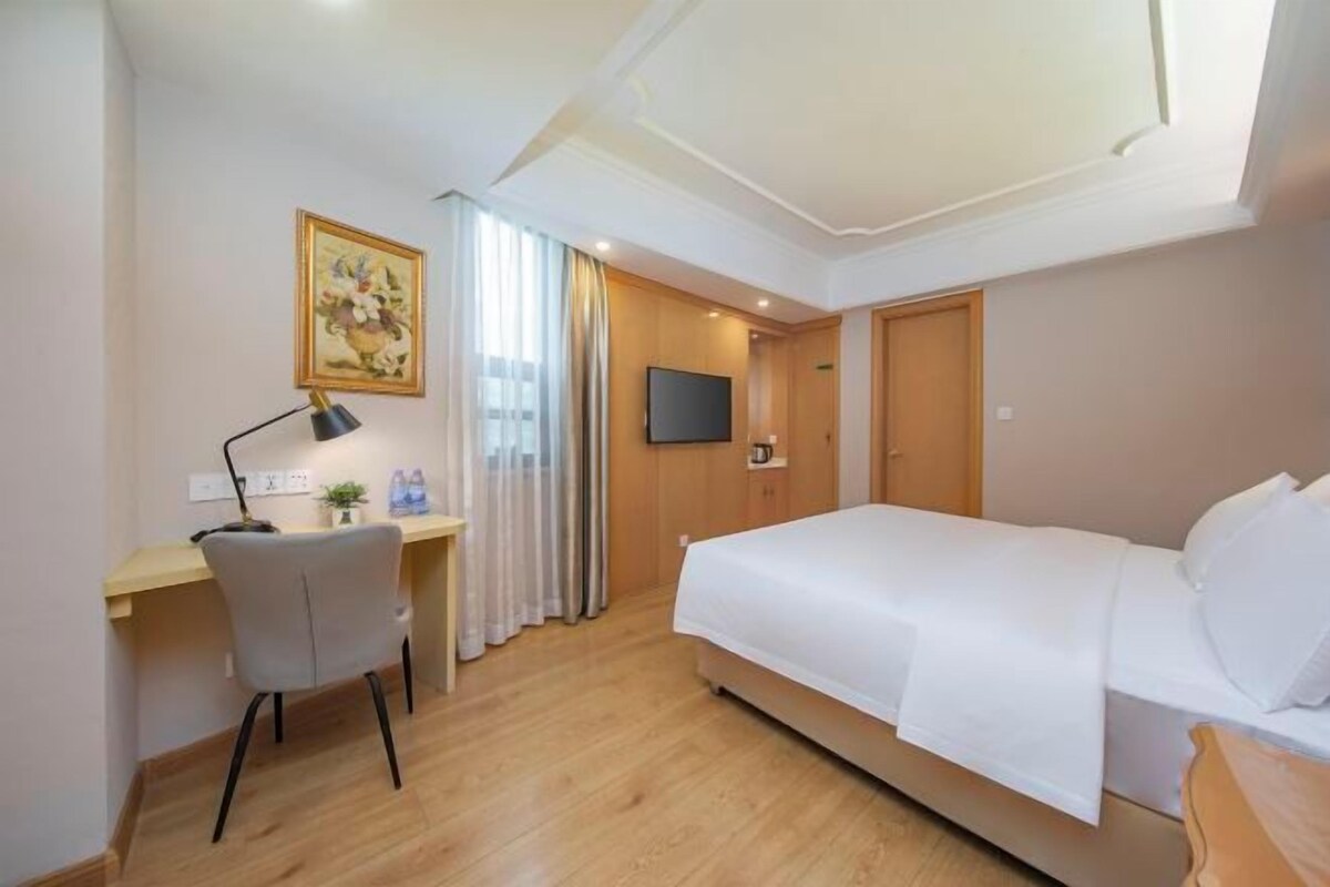 A hotel room with a bed, a desk with a chair, a television, and a painting on the wall.