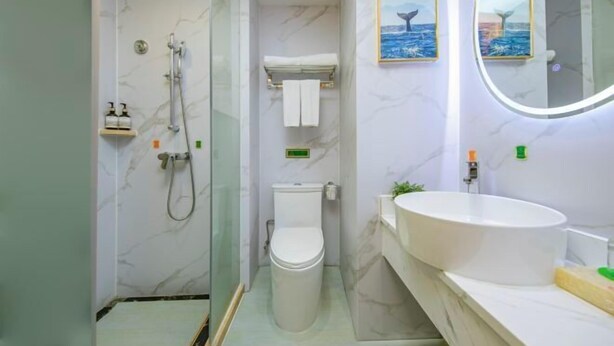 A bathroom with a shower, toilet, sink, and two framed pictures on the wall. - Vienna International Hotel (Fuzhou)