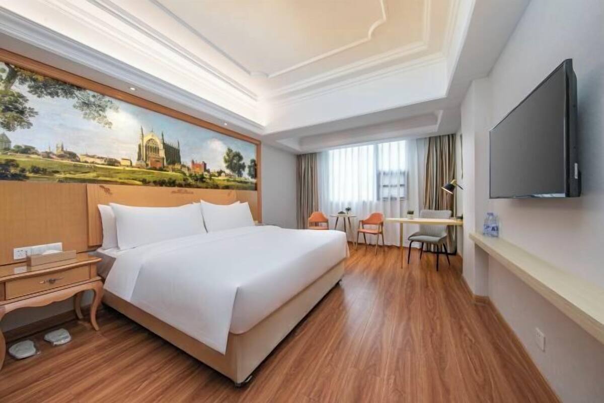A hotel room with a large bed, a desk, a chair, a television, and a painting on the wall.