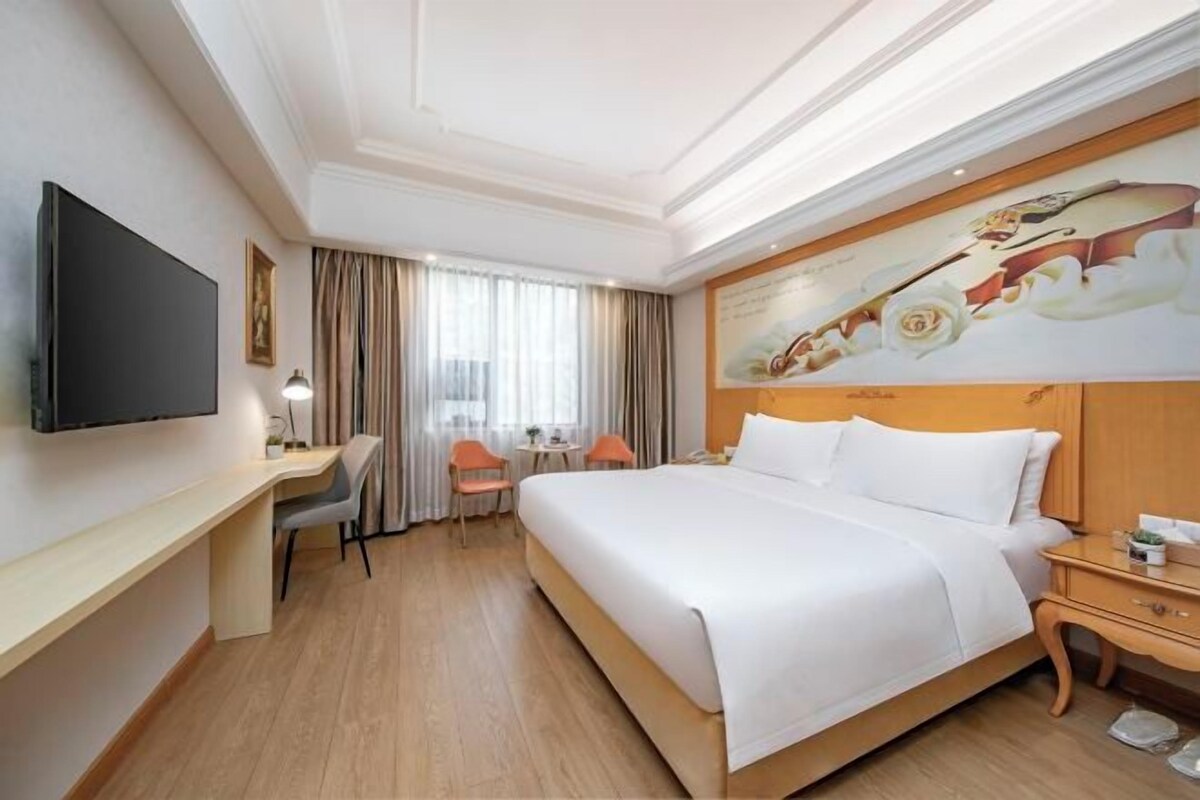 A hotel room with a large bed, a desk, a chair, a TV, and a painting on the wall.