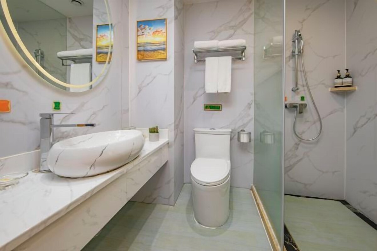 A modern bathroom with a marble vanity, a toilet, a shower, and a large mirror.