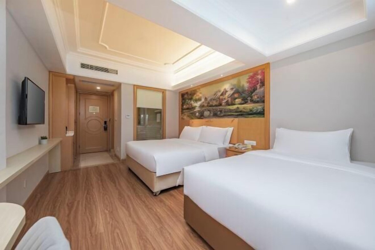 A hotel room with two beds, a painting on the wall, a TV mounted on the wall, and a wooden floor.