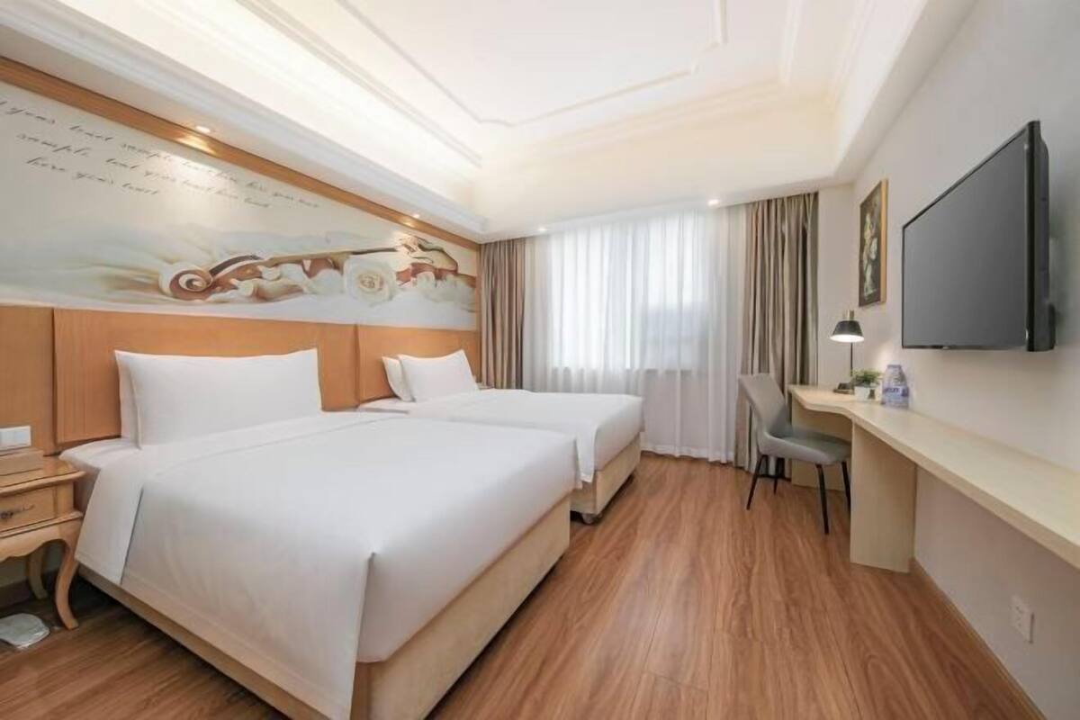 A hotel room with two beds, a desk, a chair, a flat-screen TV, and a mural on the wall.