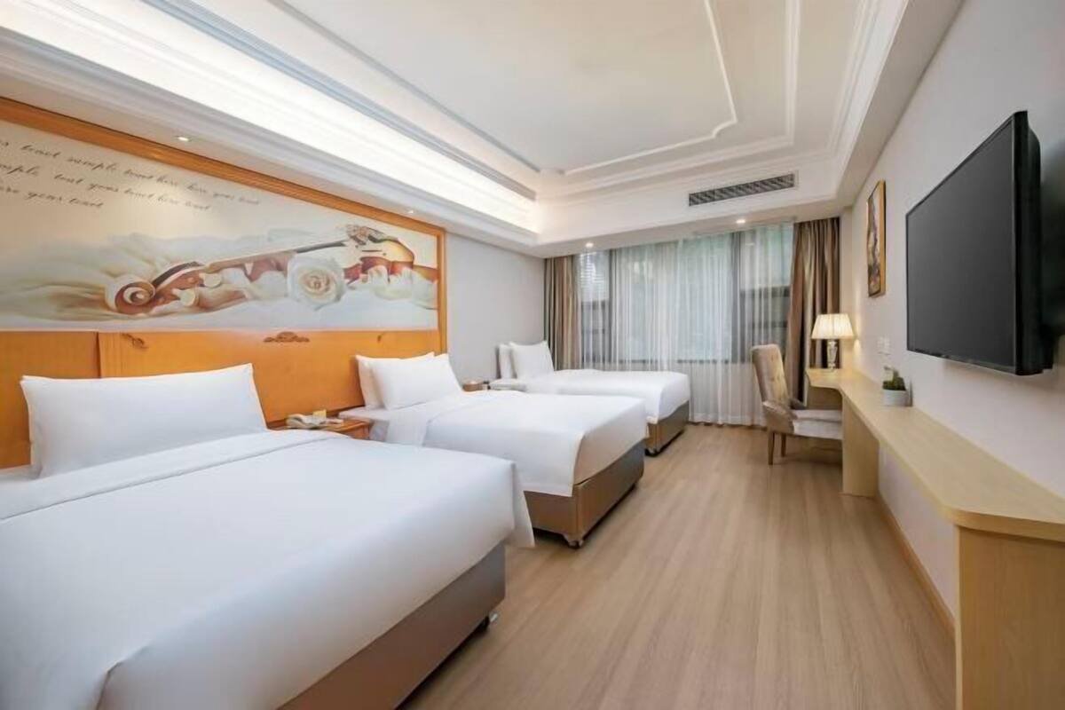 A hotel room with two beds, a flat-screen TV, a desk, and a painting on the wall.