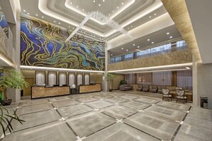 A spacious lobby with a marble floor, a reception desk, and a large wall mural. - Huacai Hotel (Wuyishan)