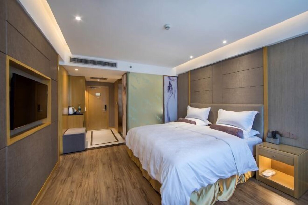 A modern hotel room with a large bed, a bedside table, a TV, and a bathroom with a shower and toilet.