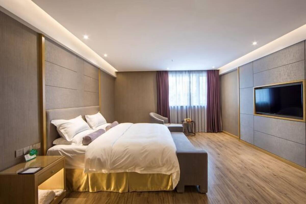 A modern hotel room with a large bed, bedside tables, a seating area, and a TV mounted on the wall.