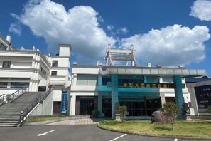 A building with a prominent entrance, a staircase leading up to the main entrance, and a large sign above the doors. - Huacai Hotel (Wuyishan)