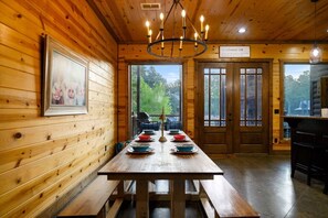 A wooden interior with a long dining table set for six, a chandelier, and a sign indicating a farmhouse-style room. - Whistling Duck · Stocked Pond: Gameroom, Shuffleboard, & Hot Tub (Broken Bow)