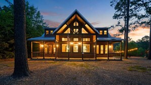 A log cabin-style building with a prominent gable roof, large windows, and a gravel driveway. - Whistling Duck · Stocked Pond: Gameroom, Shuffleboard, & Hot Tub (Broken Bow)