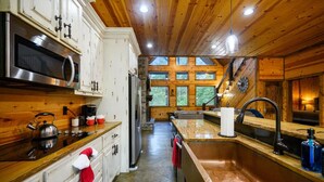 A kitchen with wooden cabinets, stainless steel appliances, a large window, and a view of the outdoors. - Whistling Duck · Stocked Pond: Gameroom, Shuffleboard, & Hot Tub (Broken Bow)