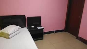 A small room with a bed, a nightstand, a door, and a pink wall.